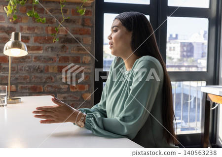 Woman speaking, gesturing hands at white desk in modern office with glass of water Woman speaking, gesturing hands at white desk in modern office with glass of water 140563238