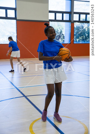 Diverse female teenage teammates practicing basketball in high school gym with basketballs 140563243