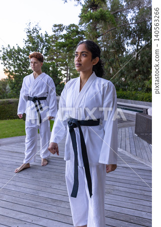 Diverse martial arts partners standing ready on wooden deck wearing gis, black belts, copy space Diverse martial arts partners standing ready on wooden deck wearing gis, black belts, copy space 140563266