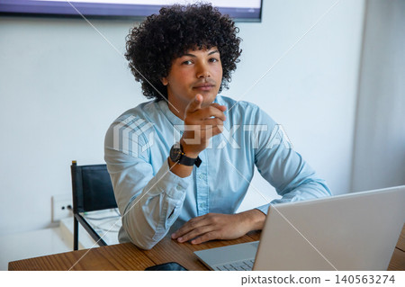 African american man in shirt pointing at camera while sitting at office with laptop phone African american man in shirt pointing at camera while sitting at office with laptop phone 140563274
