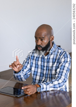 Mature african american man sitting at table in home office wearing watch and using tablet Mature african american man sitting at table in home office wearing watch and using tablet 140563292
