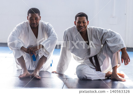 African american training partners sitting on mats in martial arts gym in white gis and belts African american training partners sitting on mats in martial arts gym in white gis and belts 140563326