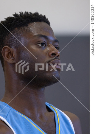 African american male athlete sweating, gazing right in gym wearing sleeveless sports jersey African american male athlete sweating, gazing right in gym wearing sleeveless sports jersey 140563334