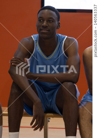 African american male basketball player sitting on wooden bench at court wearing blue jersey 140563337