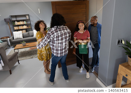 Diverse friends greeting each other at modern home entryway by wooden front door with gift bag Diverse friends greeting each other at modern home entryway by wooden front door with gift bag 140563415