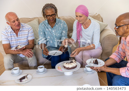 Diverse friends sharing chocolate cake on white coffee table in living room with cups Diverse friends sharing chocolate cake on white coffee table in living room with cups 140563473