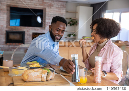 African american couple at wooden dining table at home having breakfast with avocado toast African american couple at wooden dining table at home having breakfast with avocado toast 140563488
