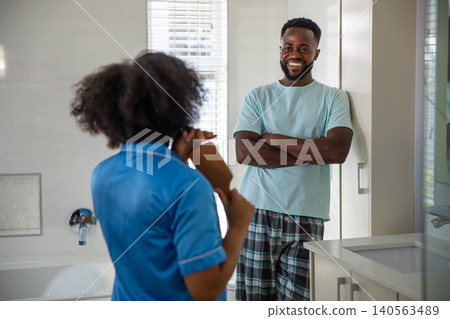 Diverse couple standing in home bathroom brushing curly hair with hairbrush, smiling Diverse couple standing in home bathroom brushing curly hair with hairbrush, smiling 140563489