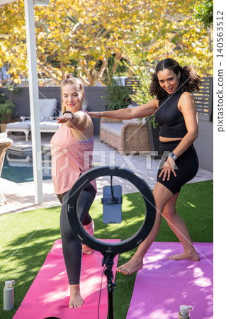 Diverse women practicing pose on backyard patio with ring light smartphone mount Diverse women practicing pose on backyard patio with ring light smartphone mount 140563512
