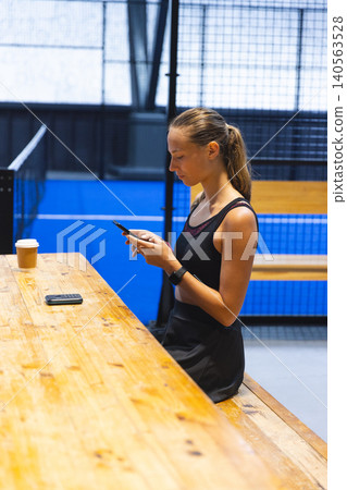 Female athlete standing by table at court checking smartphone near coffee cup and second phone Female athlete standing by table at court checking smartphone near coffee cup and second phone 140563528