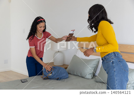 Diver mom offering passport and boarding pass to teenage daughter packing blue backpack Diver mom offering passport and boarding pass to teenage daughter packing blue backpack 140564121