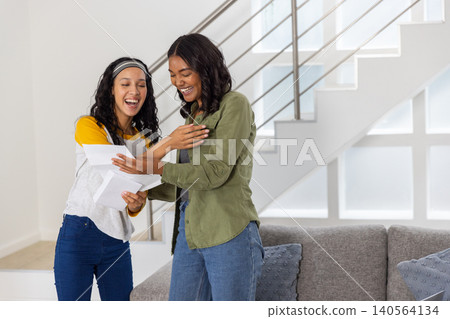 Diverse mom and teenage daughter smiling while holding opened envelopes and papers Diverse mom and teenage daughter smiling while holding opened envelopes and papers 140564134