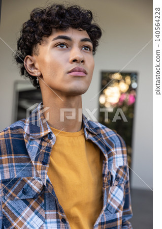 Asian man gazing upward at building entrance wearing yellow t-shirt, cross earring, shirt Asian man gazing upward at building entrance wearing yellow t-shirt, cross earring, shirt 140564228