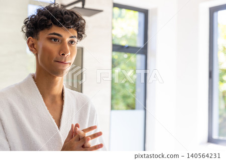 Middle eastern man applying skincare product in bathroom with bathrobe and framed windows 140564231
