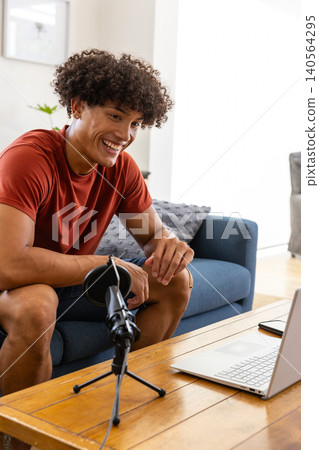African american man sitting on sofa in living room recording podcast with microphone, laptop African american man sitting on sofa in living room recording podcast with microphone, laptop 140564295