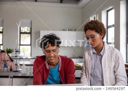 African American instructor and teenage student using laptop, wearing safety goggles in school lab African American instructor and teenage student using laptop, wearing safety goggles in school lab 140564297