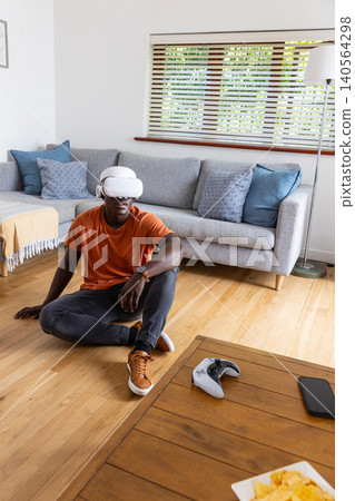 African american man wearing vr headset holding vr controller on floor in living room African american man wearing vr headset holding vr controller on floor in living room 140564298