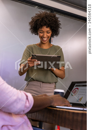 Diverse coworkers collaborating on laptop and tablet in office meeting nook with coffee cup Diverse coworkers collaborating on laptop and tablet in office meeting nook with coffee cup 140564318