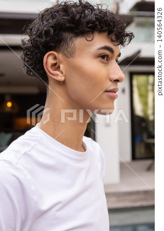 Man standing on wooden pool deck by glass doors wearing t-shirt and hoop earrings Man standing on wooden pool deck by glass doors wearing t-shirt and hoop earrings 140564326