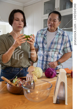 Diverse couple examining lettuce, slicing cabbage with mandoline slicer on kitchen countertop Diverse couple examining lettuce, slicing cabbage with mandoline slicer on kitchen countertop 140564340