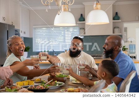 African American family raising glasses of milk at wooden dining table with salad African American family raising glasses of milk at wooden dining table with salad 140564342