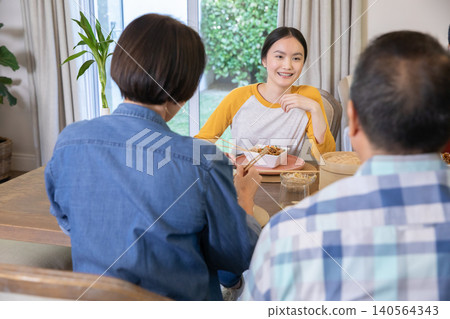 Asian family sitting around dining table at home sharing meal with bento box and chopsticks Asian family sitting around dining table at home sharing meal with bento box and chopsticks 140564343