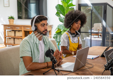 Diverse coworkers producing podcast in home studio using microphones, laptops and headphones Diverse coworkers producing podcast in home studio using microphones, laptops and headphones 140564350
