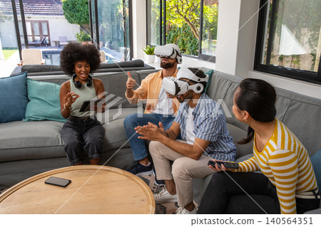 Diverse friends playing virtual reality games in living room on sofa with tablet a Diverse friends playing virtual reality games in living room on sofa with tablet a 140564351