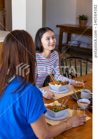 Asian mother and daughter eating noodle soup with chopsticks at dining table sipping iced tea Asian mother and daughter eating noodle soup with chopsticks at dining table sipping iced tea 140564382