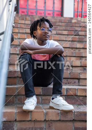 African american teenage boy leaning on rail on brick steps with glasses and white sneakers African american teenage boy leaning on rail on brick steps with glasses and white sneakers 140564427
