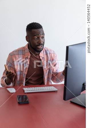 African american man gesturing at computer monitor presenting data on desk with keyboard African american man gesturing at computer monitor presenting data on desk with keyboard 140564452