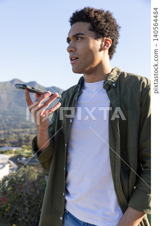 African american man recording voice note on phone standing on hill viewing valley, mountains African american man recording voice note on phone standing on hill viewing valley, mountains 140564484