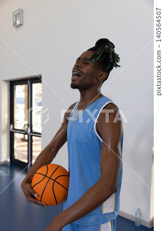 African american male wearing jersey standing on gym court holding ball sweating at exit doors African american male wearing jersey standing on gym court holding ball sweating at exit doors 140564507