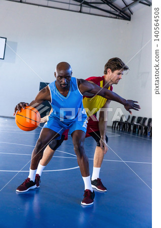 Diverse male opponents dribbling basketball, defending on blue court with chairs and court lines Diverse male opponents dribbling basketball, defending on blue court with chairs and court lines 140564508