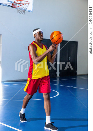 African american teenage athlete holding orange basketball at chest on court in uniform African american teenage athlete holding orange basketball at chest on court in uniform 140564514