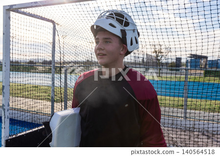 Teenage boy standing in front of goal in caged helmet and blocker pad on sports field 140564518