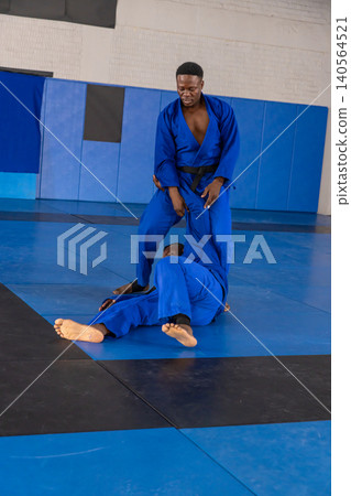 African american male training partners grappling on blue mats at martial gym with gis African american male training partners grappling on blue mats at martial gym with gis 140564521