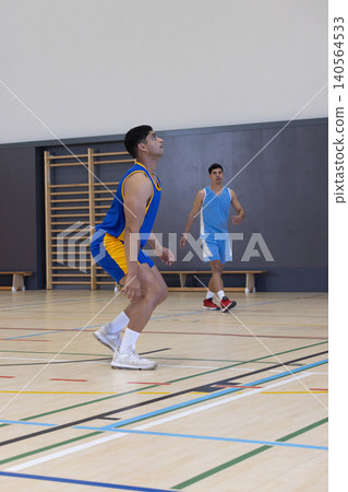 Male basketball players bending knees preparing to rebound on gym court with wall bars Male basketball players bending knees preparing to rebound on gym court with wall bars 140564533