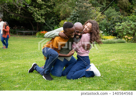 Diverse family hugging on manicured grass lawn in garden near shrubs, trampoline frame Diverse family hugging on manicured grass lawn in garden near shrubs, trampoline frame 140564568