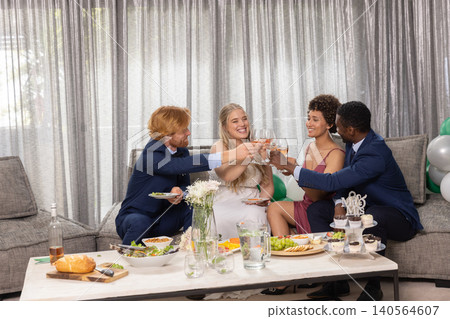 Diverse couples in formal attire clinking wine glasses, sampling appetizers in living room Diverse couples in formal attire clinking wine glasses, sampling appetizers in living room 140564607