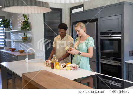 Diverse couple unpacking mesh bags of lemons, cooking oil on kitchen island under pendant lights Diverse couple unpacking mesh bags of lemons, cooking oil on kitchen island under pendant lights 140564652