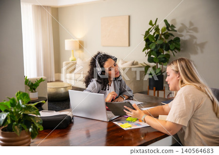 Diverse female coworkers reviewing data on laptop, tablet, color charts in home office 140564683