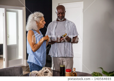 Diverse senior couple examining condiment jars at home dining table with reusable mesh bag Diverse senior couple examining condiment jars at home dining table with reusable mesh bag 140564693