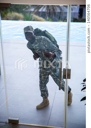 African american male soldier standing by glass door in camo uniform with backpack on pool deck 140564706