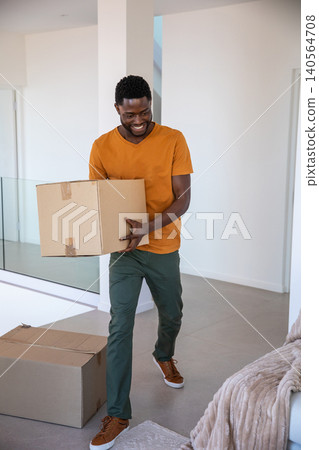 African american man carrying taped cardboard box through living space with glass railing African american man carrying taped cardboard box through living space with glass railing 140564708