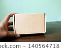 Hand Holding a Small Brown Cardboard Shipping Box 140564718