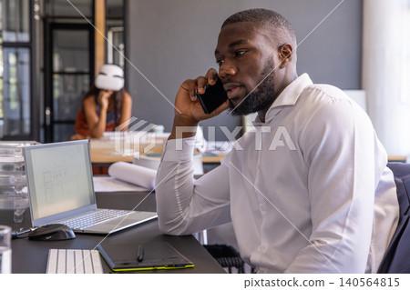 Diverse coworkers collaborating on architectural plans in studio with smartphone and safety helmet 140564815