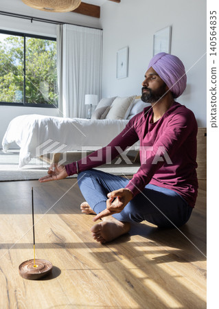 Indian man wearing turban meditating on bedroom floor with incense stick, copy space Indian man wearing turban meditating on bedroom floor with incense stick, copy space 140564835