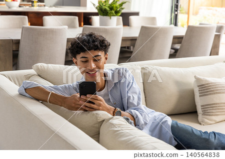 Man holding smartphone while reclining on sectional couch in living room with cushions Man holding smartphone while reclining on sectional couch in living room with cushions 140564838