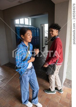 Diverse classmates standing and chatting in school hallway near blue lockers holding smartphone Diverse classmates standing and chatting in school hallway near blue lockers holding smartphone 140564878